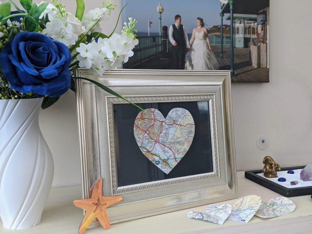 My finished love map inside a frame next to a vase of faux flowers and a photo of my husband and I are on our wedding day